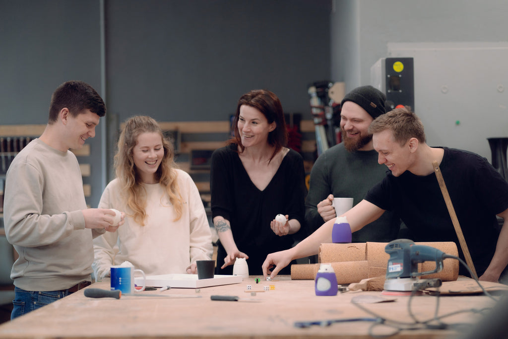 The TukToro team stands laughing at a workbench and assembling a TukToro figure together: Andreas Härung, Annabell Terrahe, Justyna Zubrycka, Patrick Goehl, Elisha Benner.