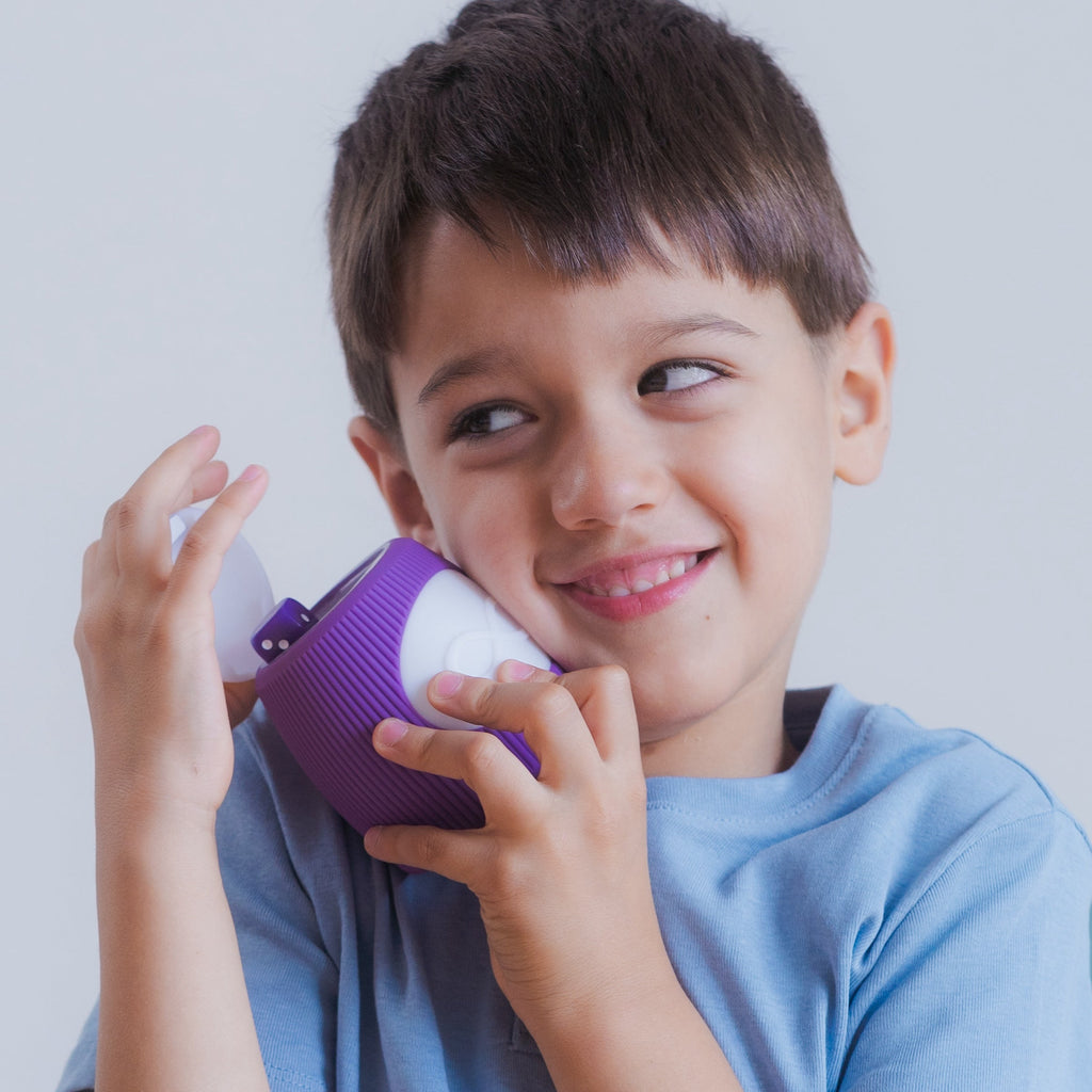 Smiling boy of pre-school age holds an unfolded TukToro figure in his arms and looks mischievously to the side.